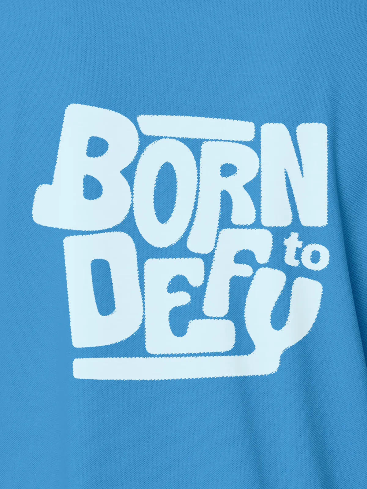 Close up of 'Born To Defy' design on Women's Blue Polo T-shirt, highlighting intricate details and vibrant print.