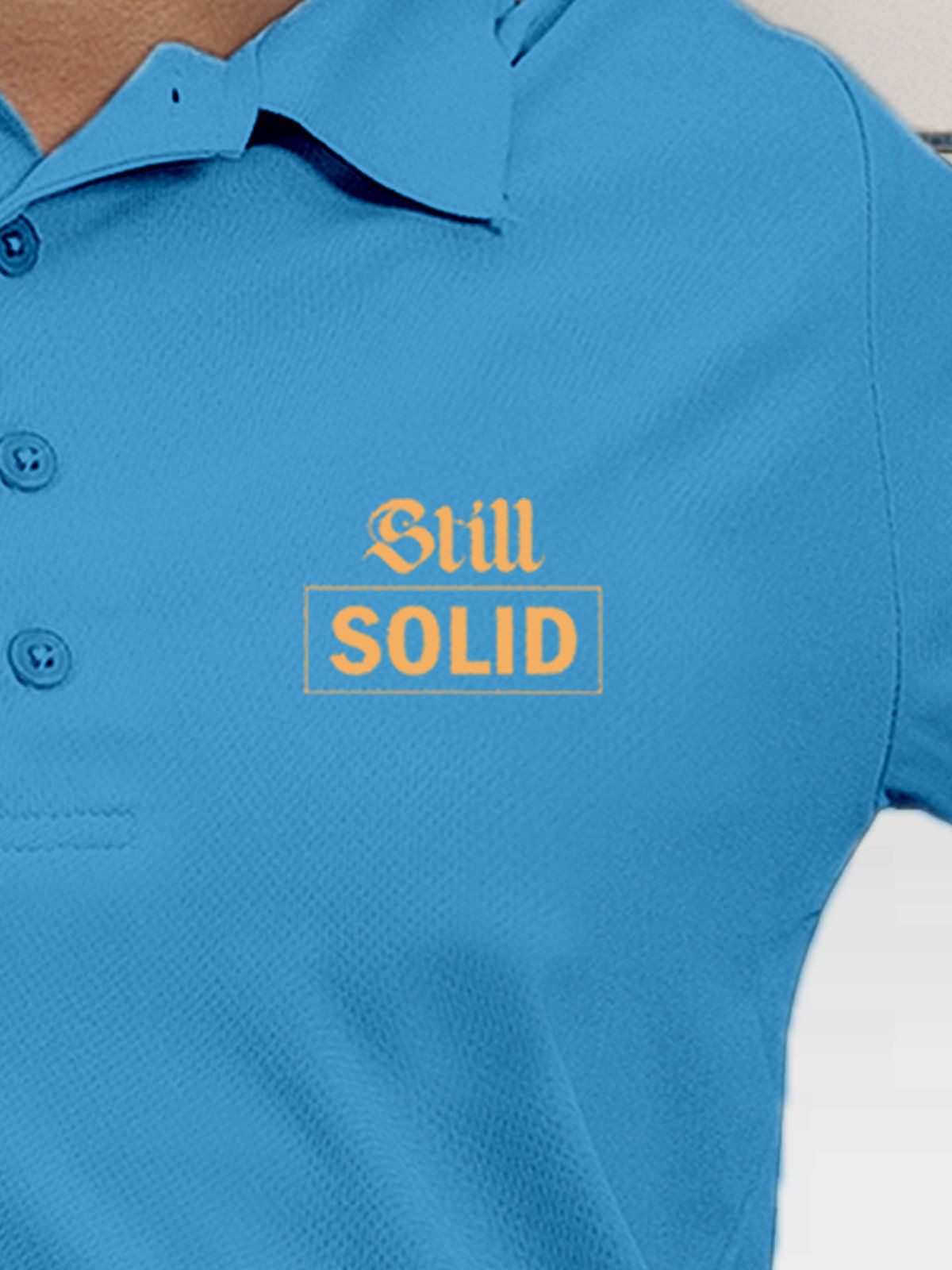 Close up of 'Still Solid' design on Women's Blue Polo T-shirt, highlighting intricate details and vibrant print.