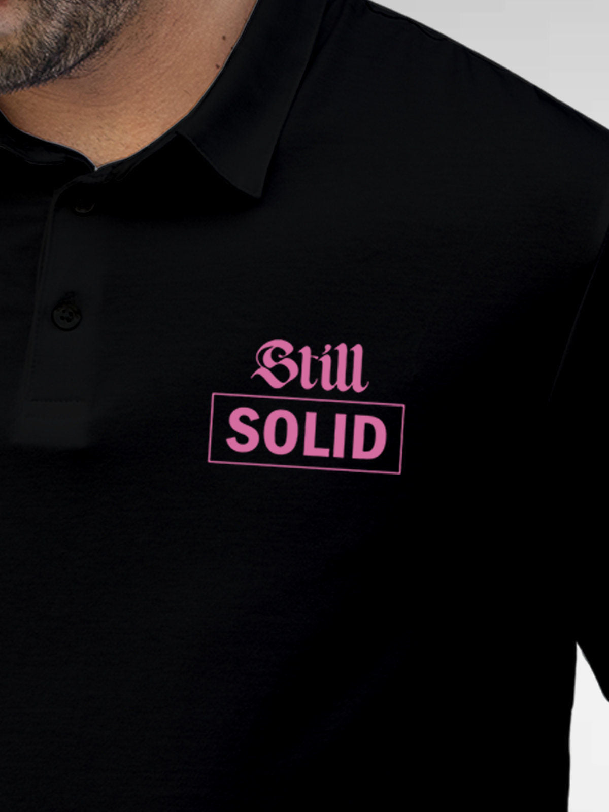 Close up of 'Still Solid' design on Men's Black Polo T-shirt, highlighting intricate details and vibrant print.