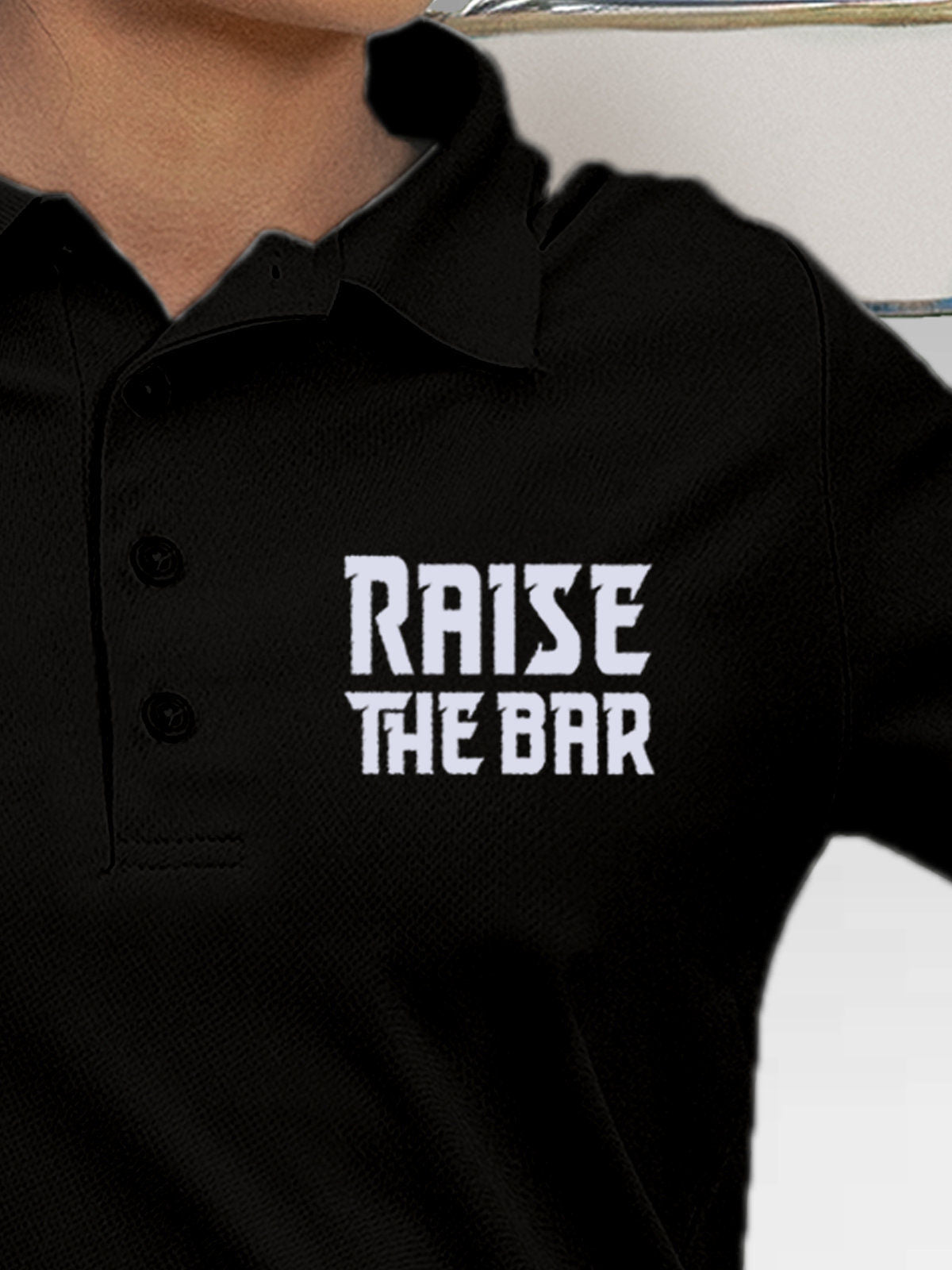 Close up of 'Raise The Bar' design on Women's Black Polo T-shirt, highlighting intricate details and vibrant print.