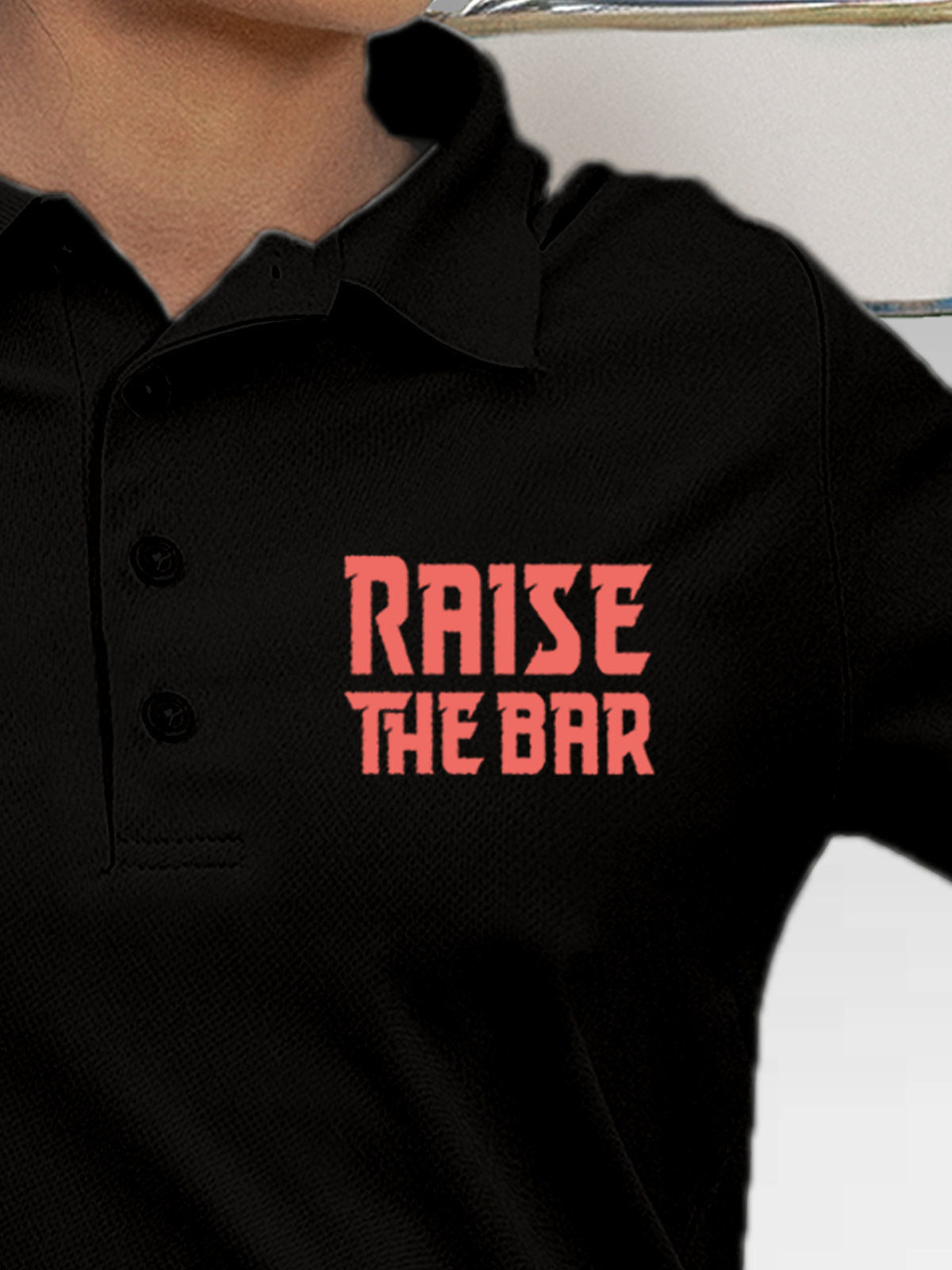 Close up of 'Raise The Bar' design on Women's Black Polo T-shirt, highlighting intricate details and vibrant print.