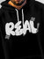 Close up of 'Real' design on Men's Black Hoodie Sweatshirt, highlighting intricate details and vibrant print.