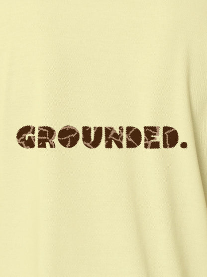 Close up of 'Grounded' design on Women's Yellow Polo T-shirt, highlighting intricate details and vibrant print.