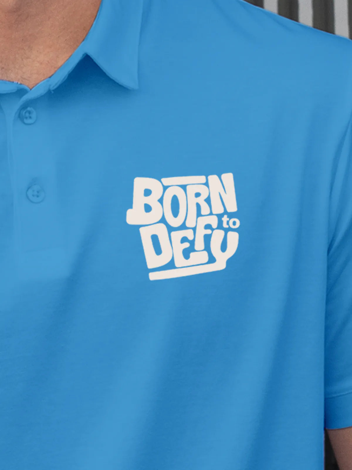 Close up of 'Born To Defy' on Men's Blue Polo T-shirt, highlighting intricate details and vibrant print.