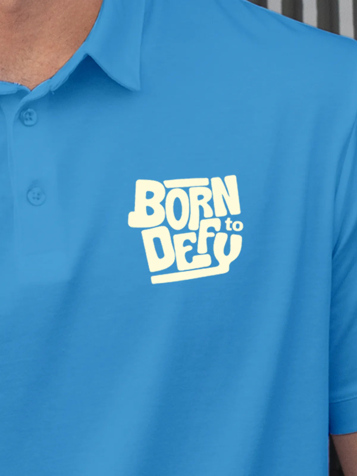 Close up of 'Born To Defy' on Men's Blue Polo T-shirt, highlighting intricate details and vibrant print.