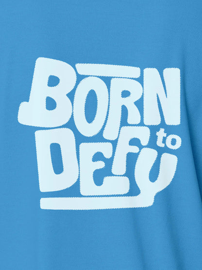 Close up of 'Born To Defy' design on Women's Blue Polo T-shirt, highlighting intricate details and vibrant print.