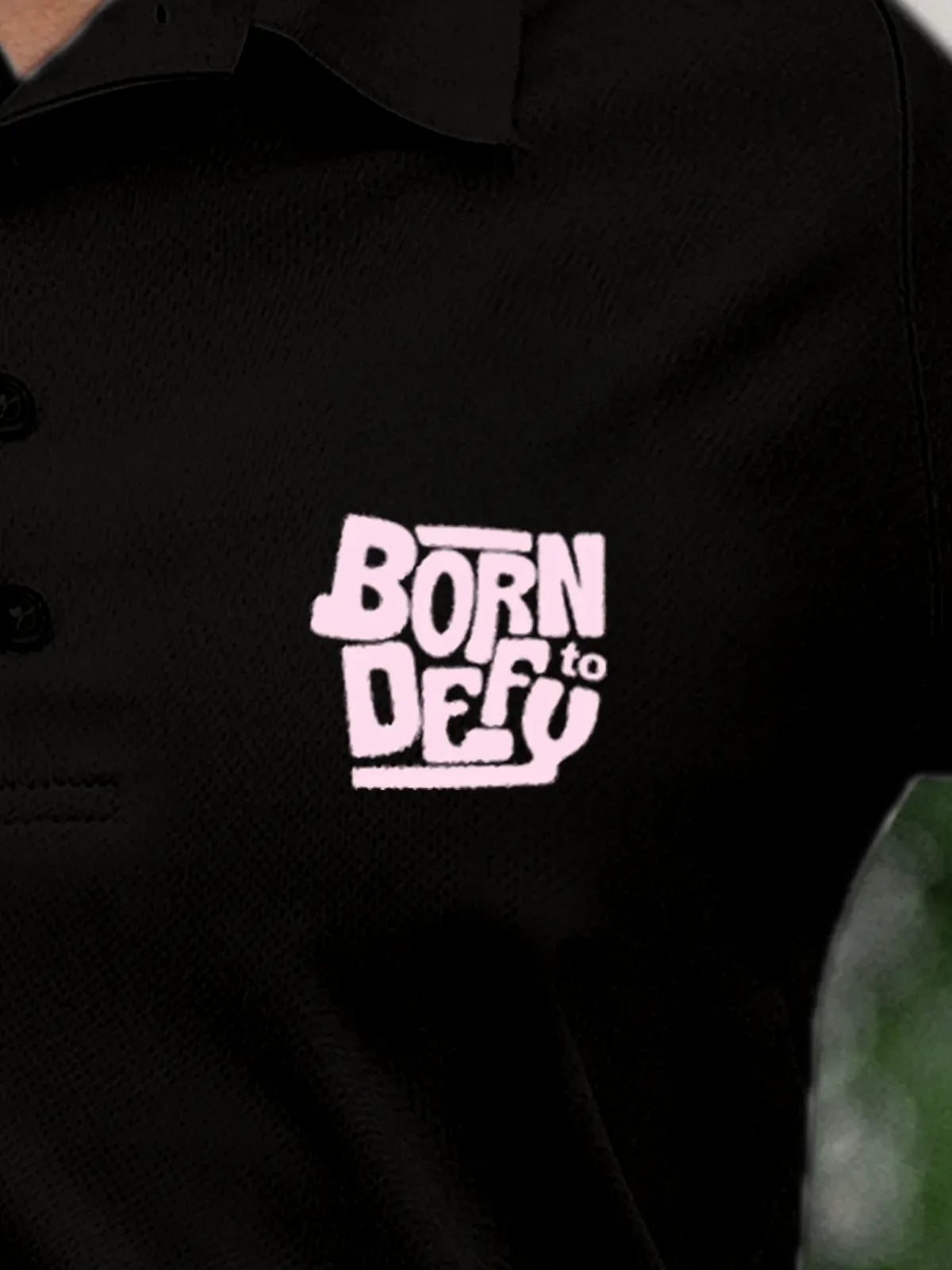 Close up of 'Born To Defy' on Women's Black Polo T-shirt, highlighting intricate details and vibrant print.