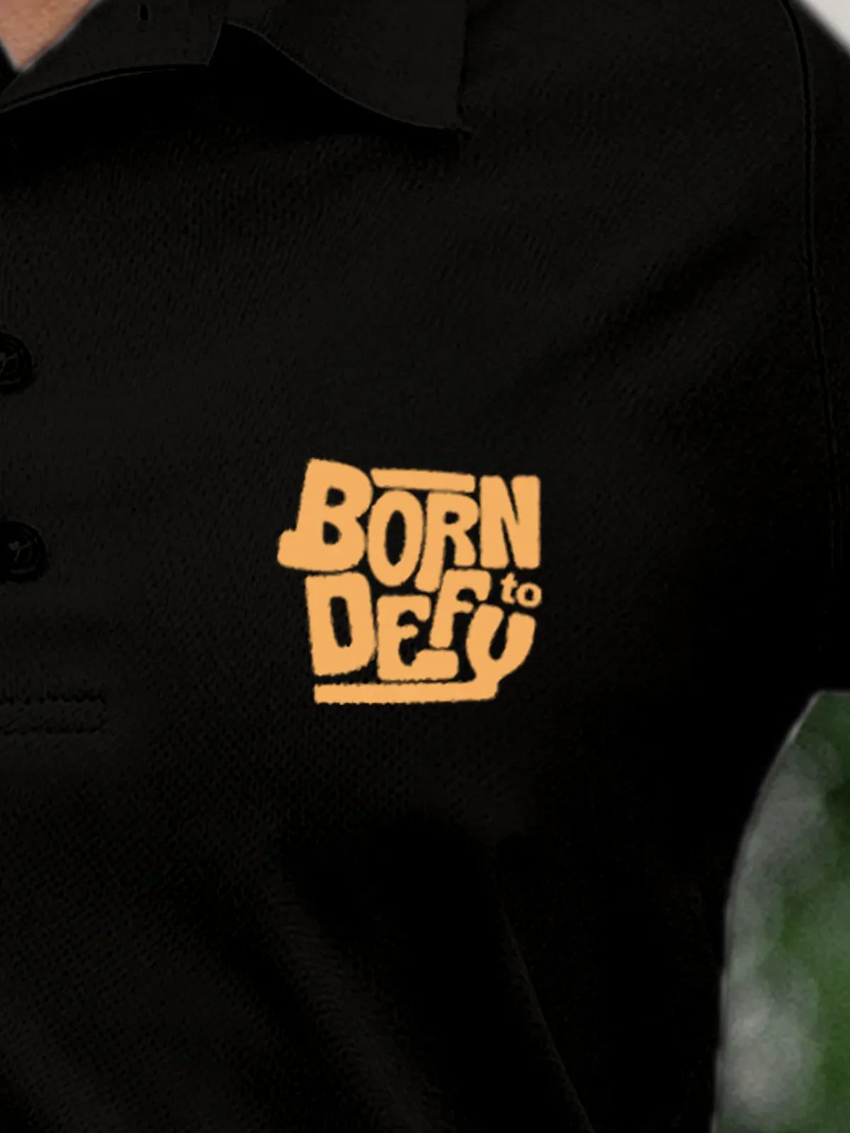 Close up of 'Born To Defy' on Women's Black Polo T-shirt, highlighting intricate details and vibrant print.
