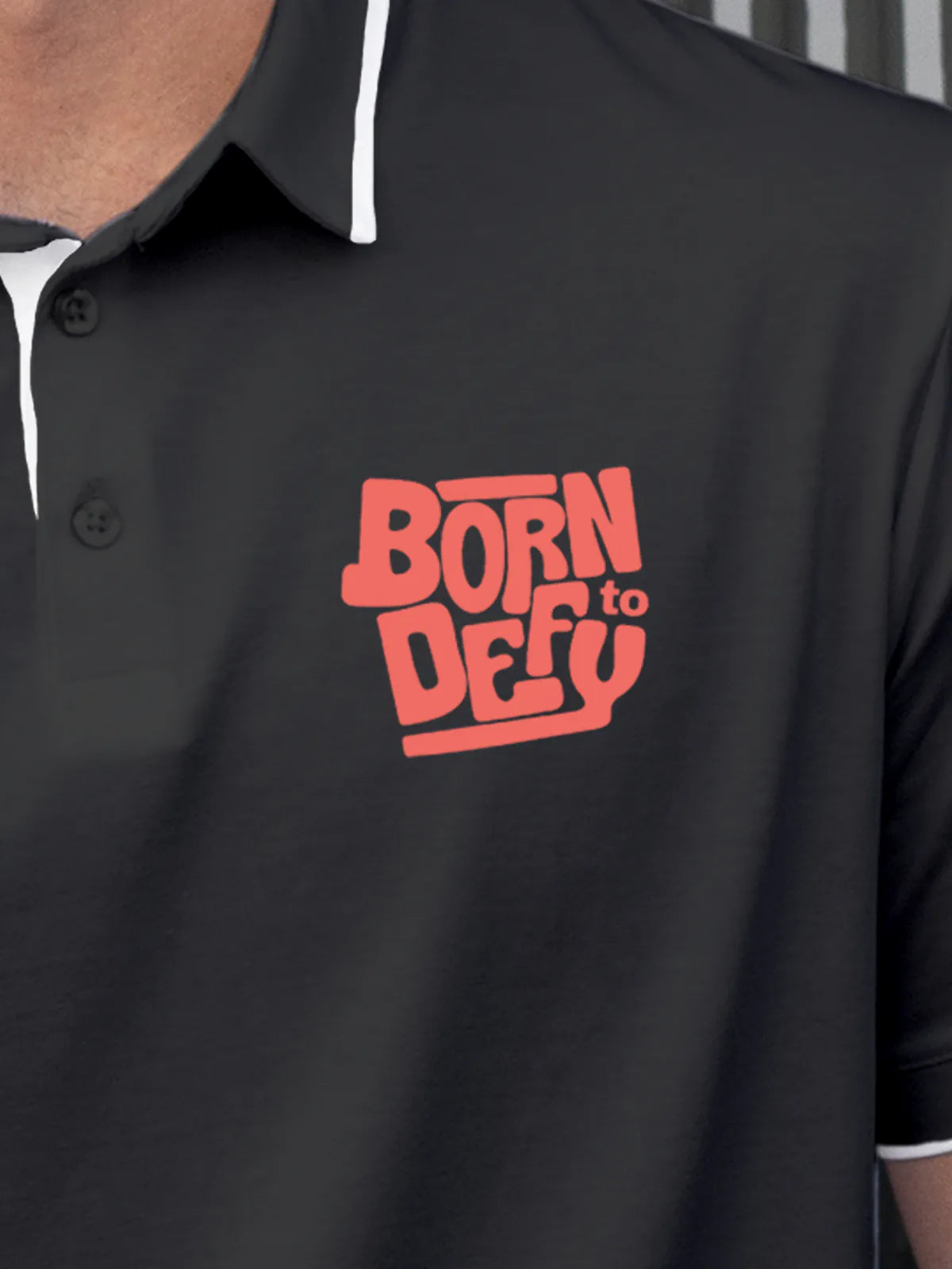 Close up of 'Born To Defy' on Men's Dark Grey Polo T-shirt, highlighting intricate details and vibrant print.