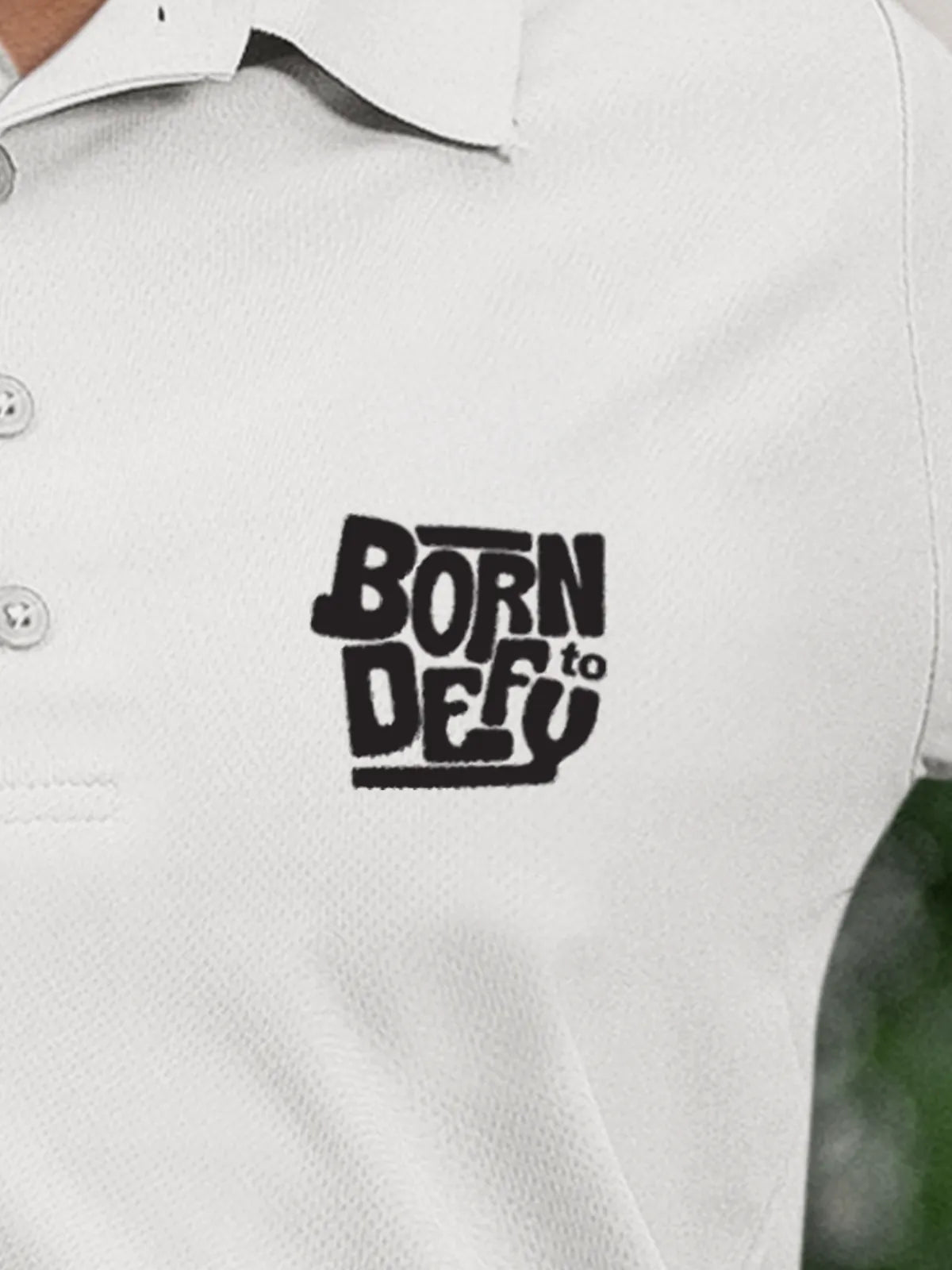 Close up of 'Born To Defy' on Women's White Polo T-shirt, highlighting intricate details and vibrant print.