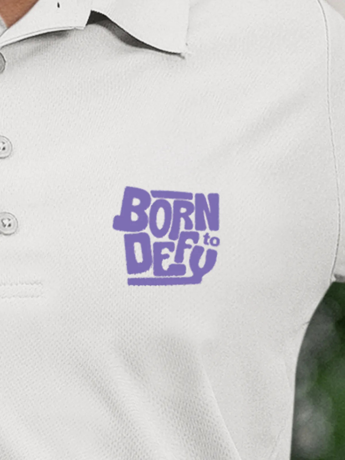 Close up of 'Born To Defy' on Women's White Polo T-shirt, highlighting intricate details and vibrant print.