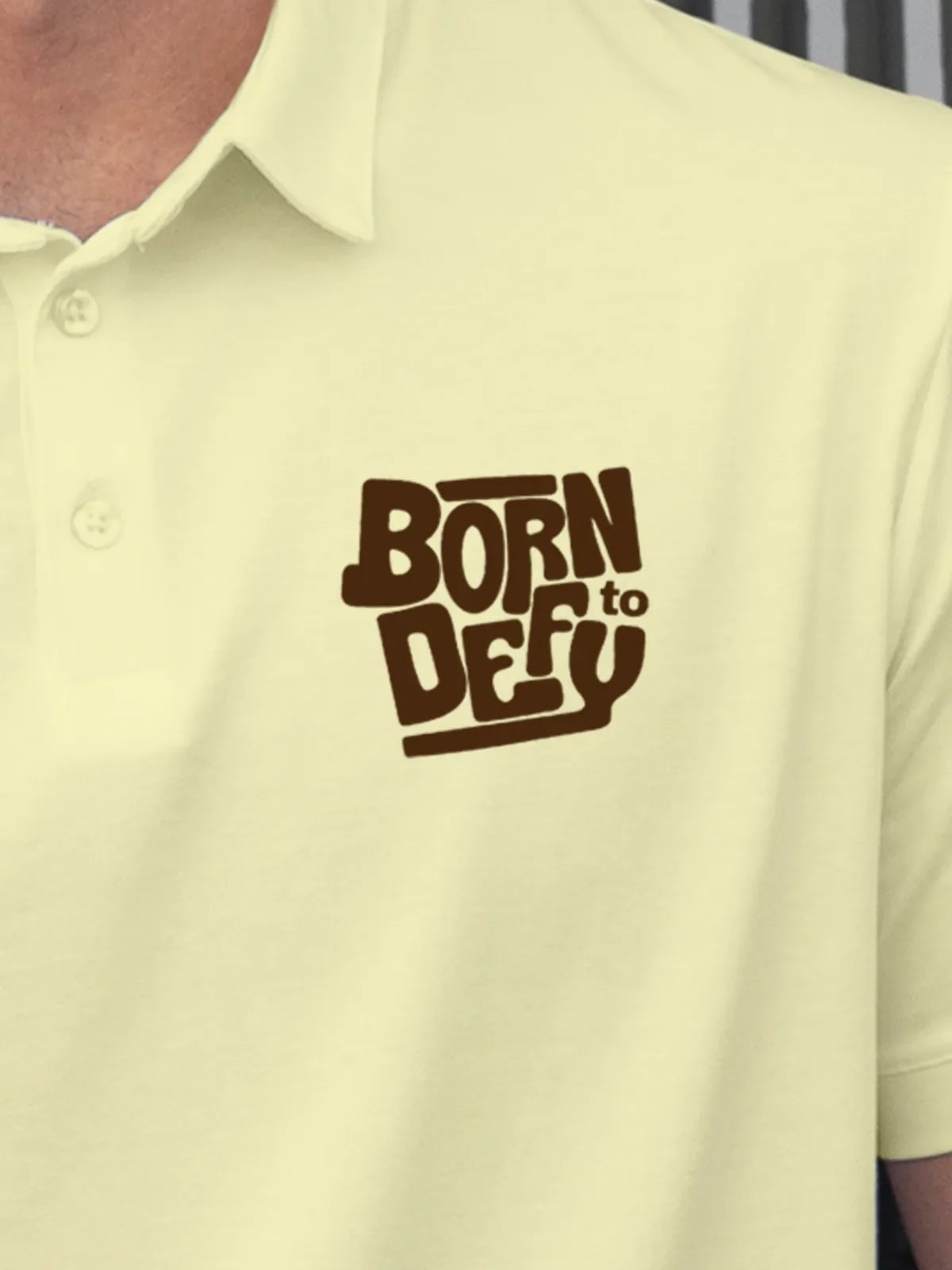 Close up of 'Born To Defy' on Men's Yellow Polo T-shirt, highlighting intricate details and vibrant print.