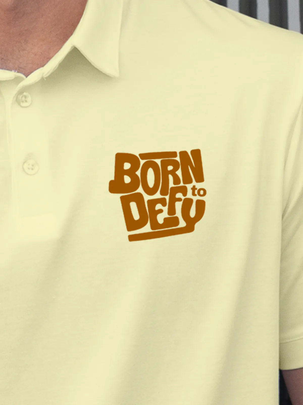Close up of 'Born To Defy' on Men's Yellow Polo T-shirt, highlighting intricate details and vibrant print.