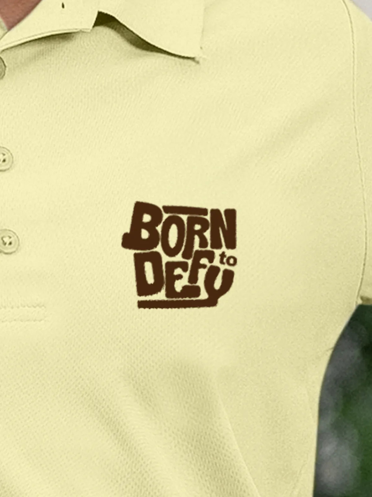 Close up of 'Born To Defy' on Women's Yellow Polo T-shirt, highlighting intricate details and vibrant print.
