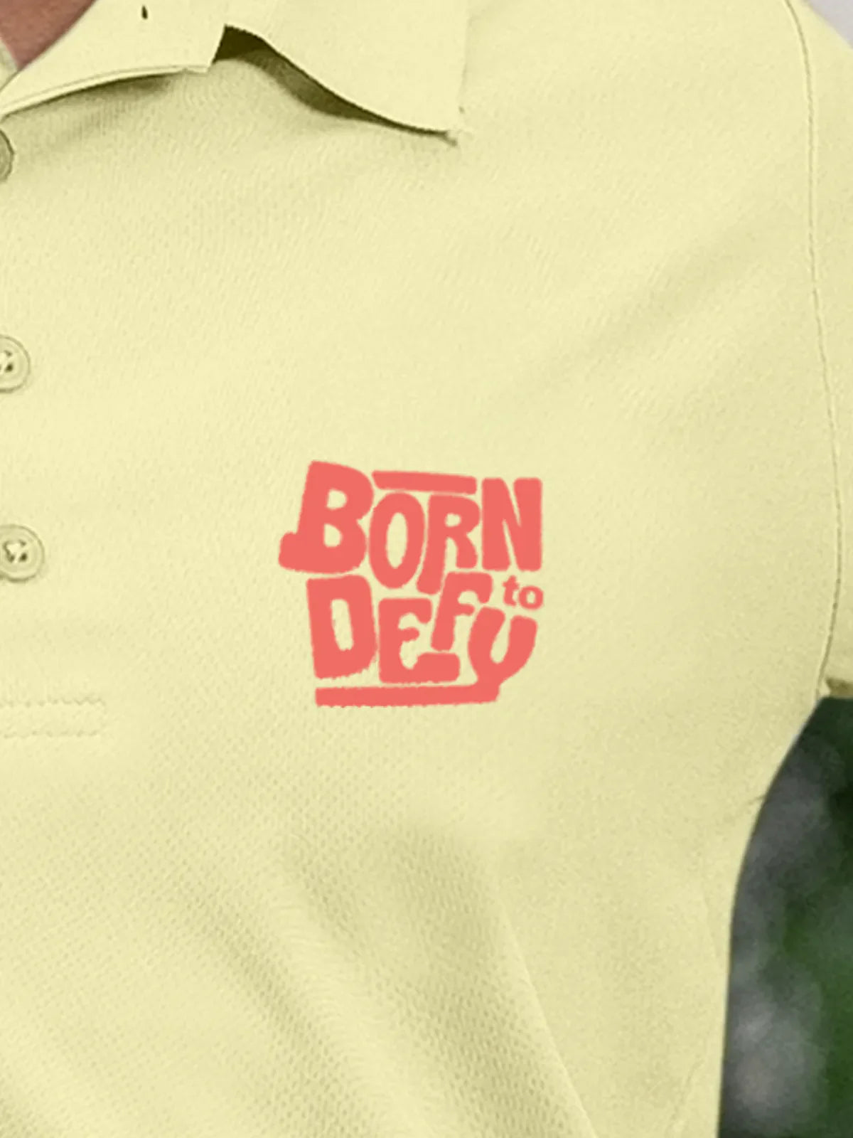 Close up of 'Born To Defy' on Women's Yellow Polo T-shirt, highlighting intricate details and vibrant print.