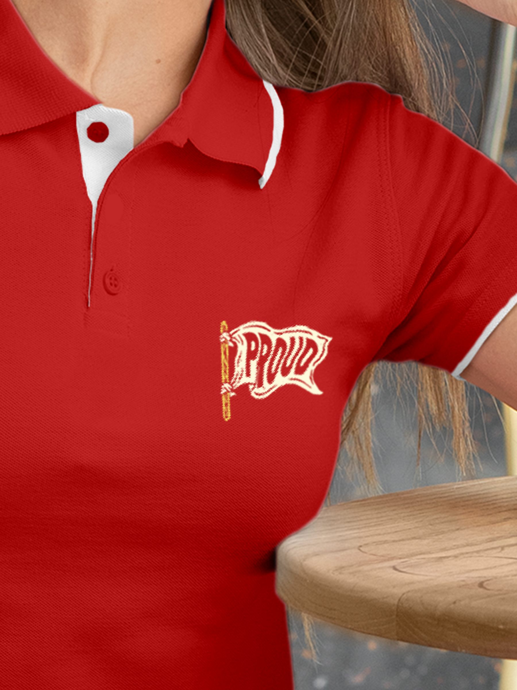 Close up of 'Proud' design on Women's Red Polo T-shirt, highlighting intricate details and vibrant print.