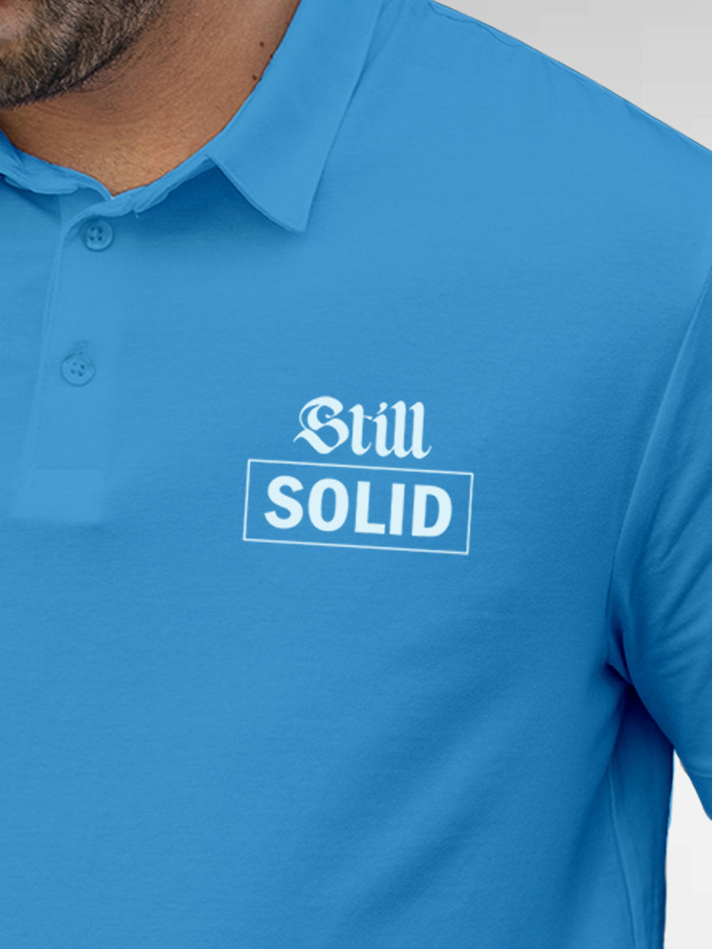 Close up of 'Still Solid' design on Men's Blue Polo T-shirt, highlighting intricate details and vibrant print.