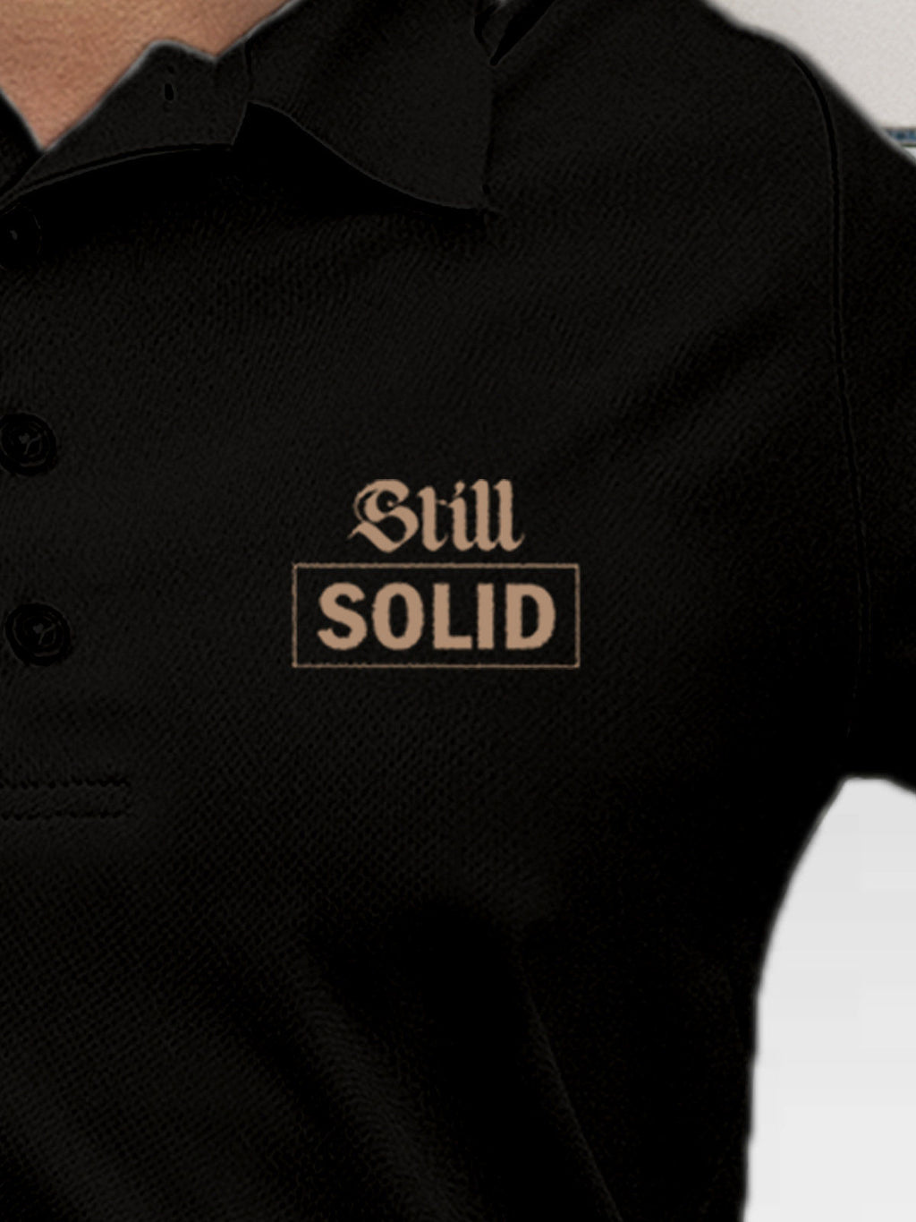Close up of 'Still Solid' design on Women's Black Polo T-shirt, highlighting intricate details and vibrant print.