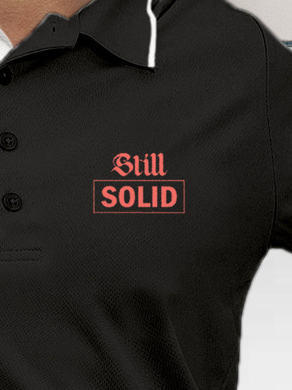 Close up of 'Still Solid' design on Women's Dark Grey Polo T-shirt, highlighting intricate details and vibrant print.