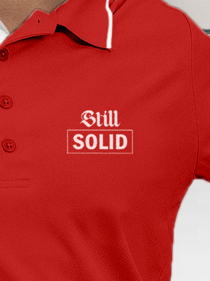 Close up of 'Still Solid' design on Women's Red Polo T-shirt, highlighting intricate details and vibrant print.