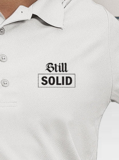 Close up of 'Still Solid' design on Women's White Polo T-shirt, highlighting intricate details and vibrant print.