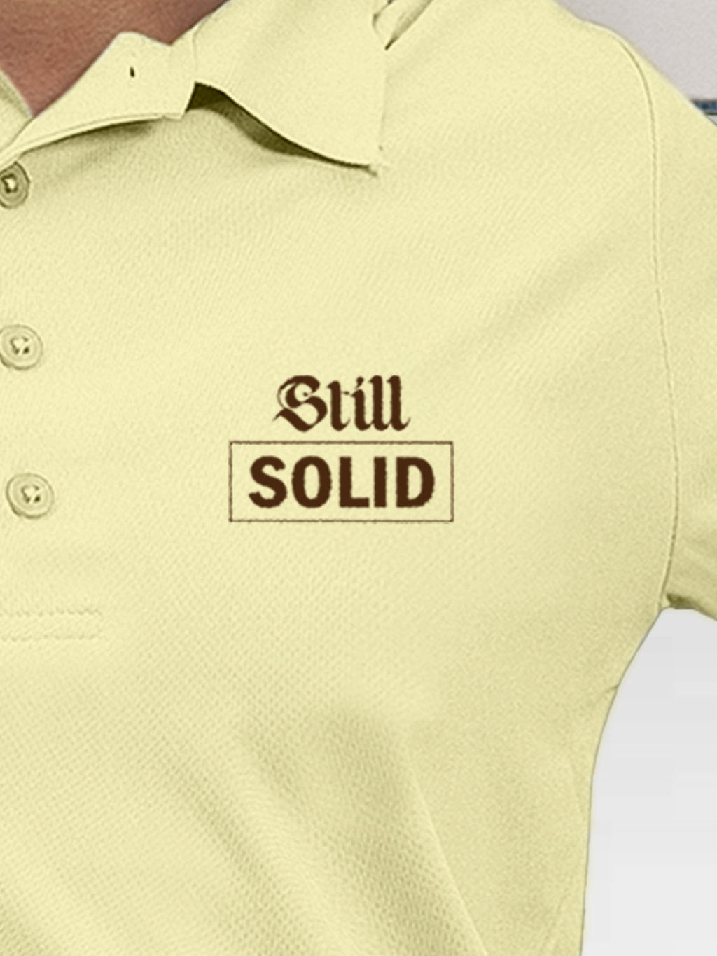 Close up of 'Still Solid' design on Women's Yellow Polo T-shirt, highlighting intricate details and vibrant print.