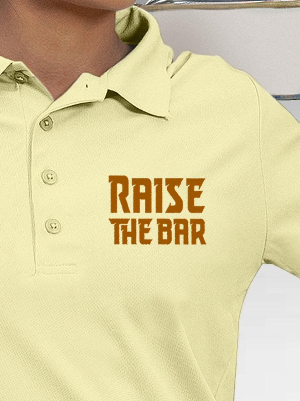 Close up of 'Raise The Bar' design on Women's Yellow Polo T-shirt, highlighting intricate details and vibrant print.